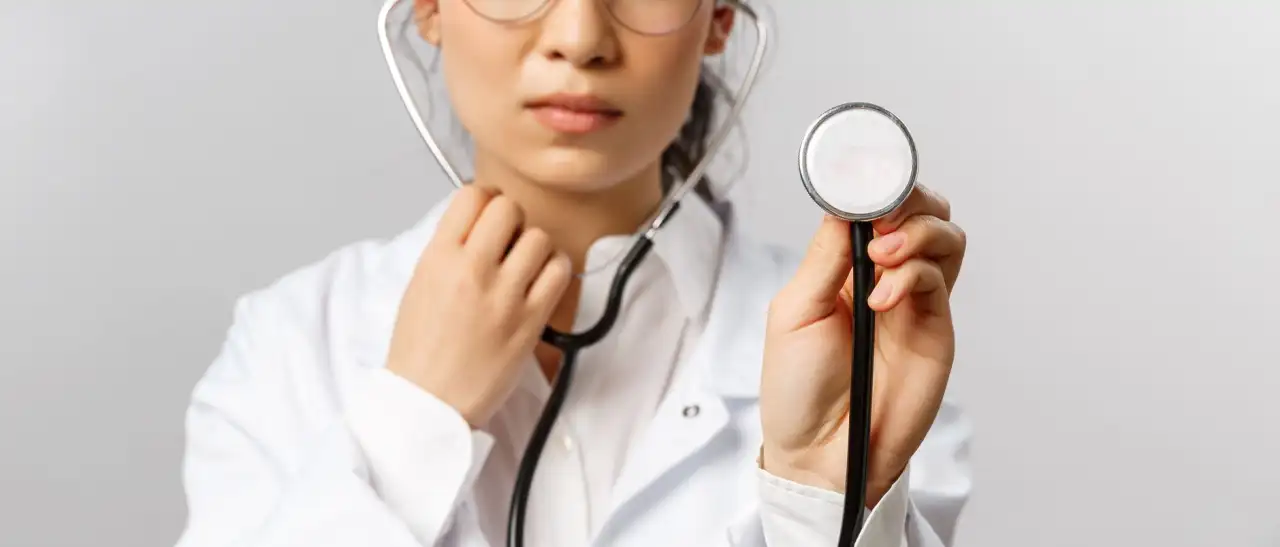 Jeune médecin en blouse blanche portant des lunettes, tenant un stéthoscope vers l'appareil photo