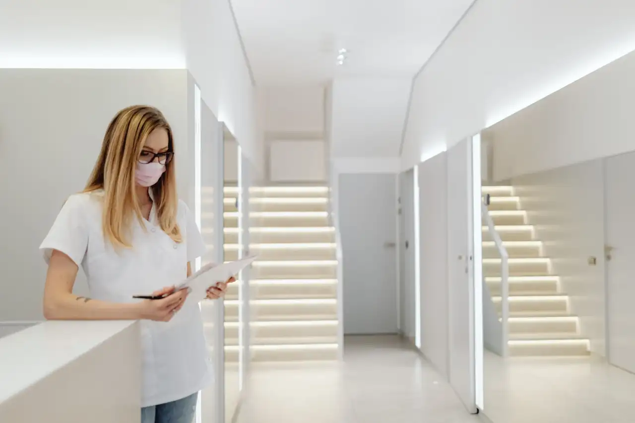 Femme avec masque et lunettes consultant une tablette dans un couloir de cabinet médical moderne